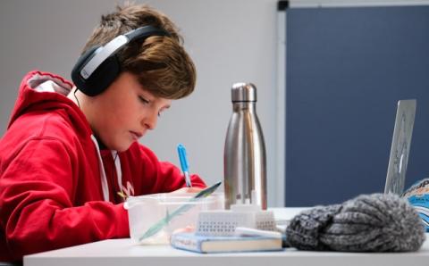 Child writing in a notebook with headphones on