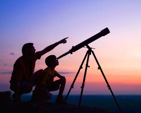image of two people looking through a telescope at night