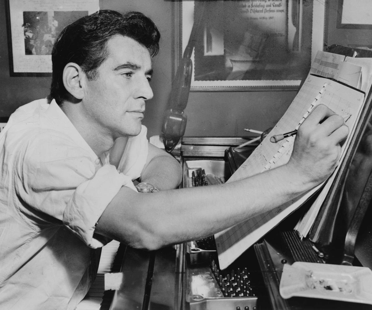 Leonard Bernstein seated at piano, making annotations to musical score - Public Domain