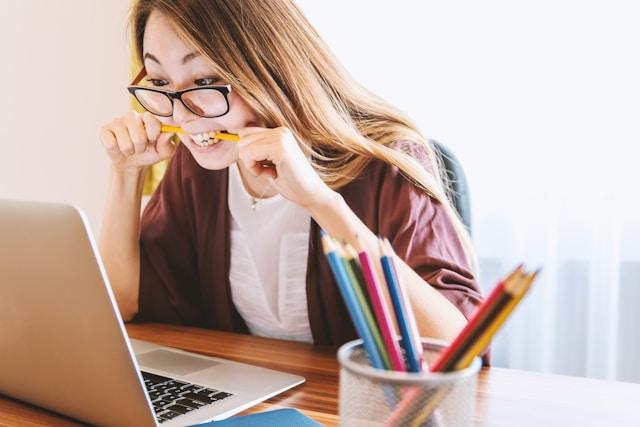 Woman biting pencil nervously looking at laptop